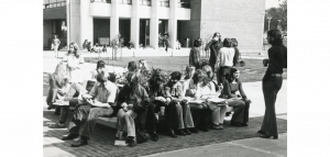 Students sitting on benches outside Building D, circa 1970-1980.